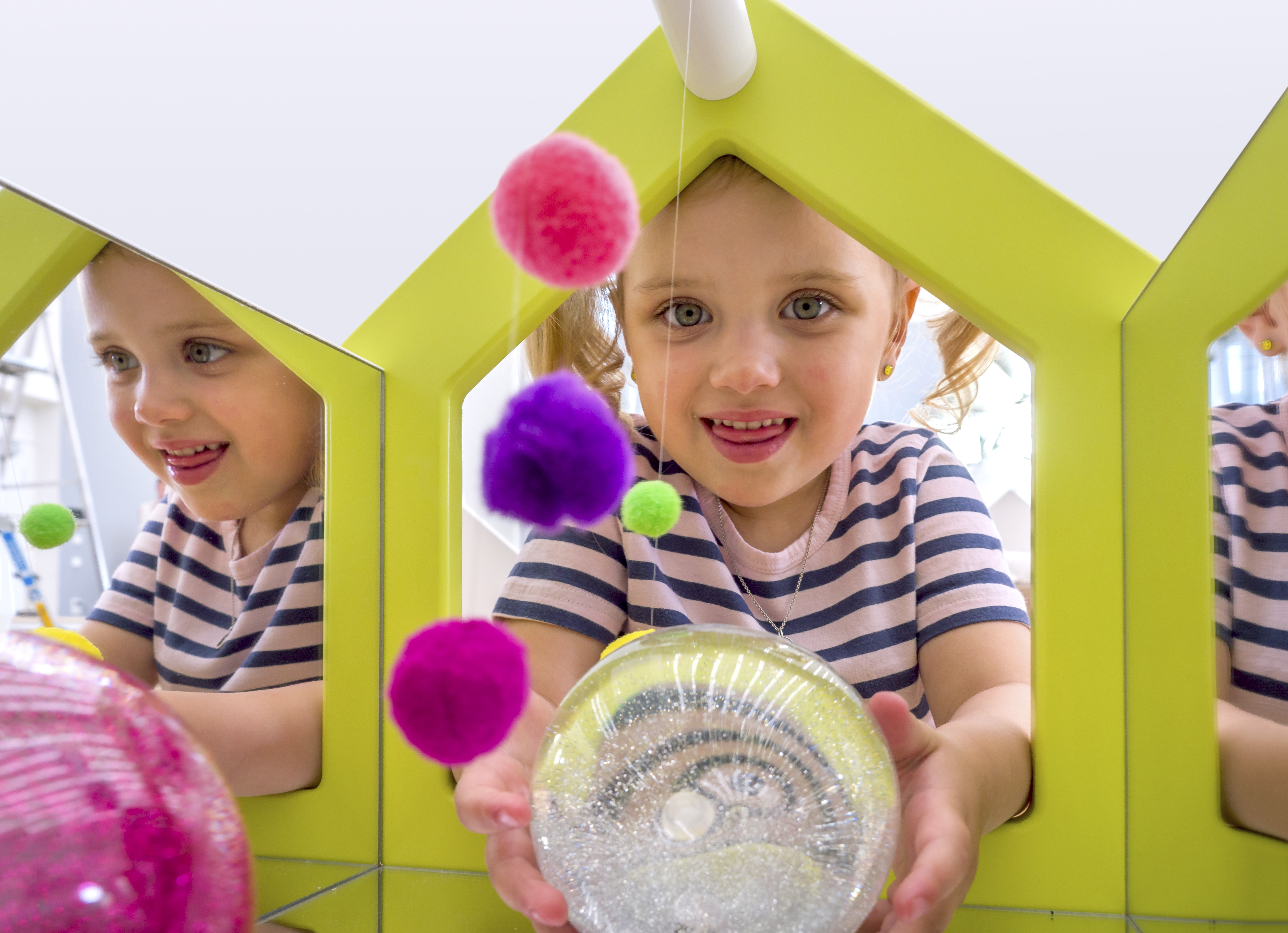 EduCasa Aufsatz Spiegelhaus mit bunten Pompoms und kleinem Mädchen mit glitzernder Kugel