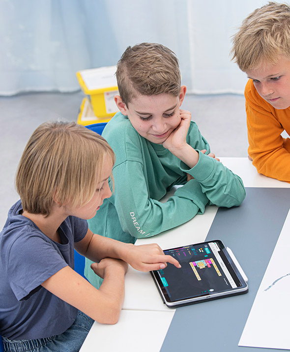 Kinder sitzen um den Tisch und machen eine Ozobot-Programmierung mit Linien und Farbcode-Magneten