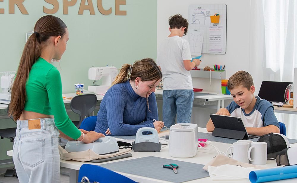 Mehrere Kinder an einem großen Tisch und jedes Kind ist mit einem anderen Arbeitsschritt des Plotterns beschäftigt