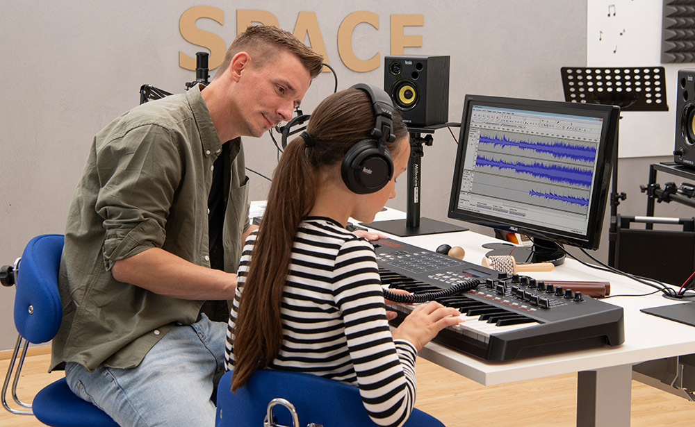 Kind sitz vor einem Keyboard und die Lehrkraft sitz daneben