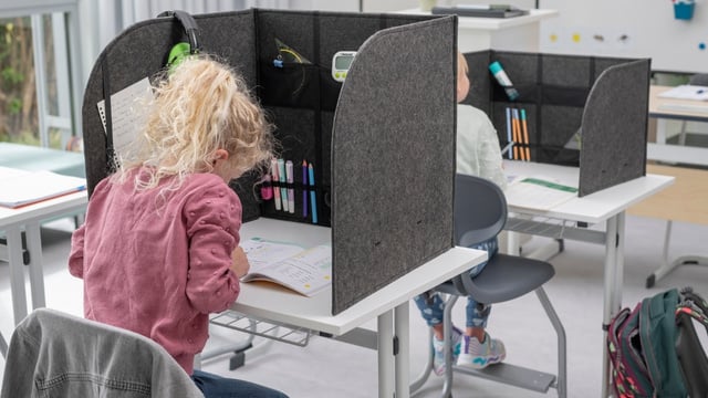 Mädchen sitzt im Unterricht an Tisch mit Trennwand