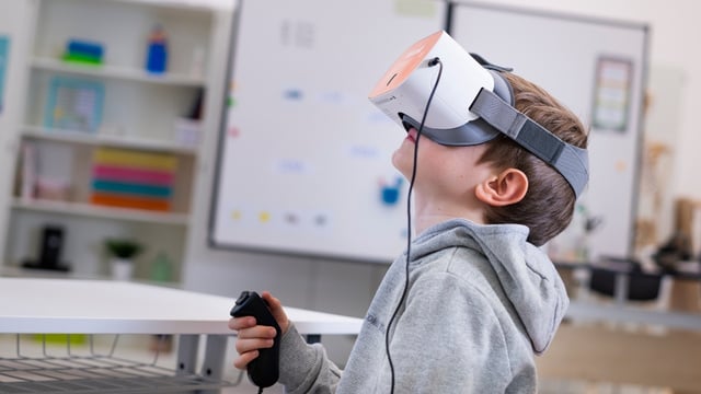 Junge sitzt im Klassenzimmer und hat ein Headset aufgesetzt