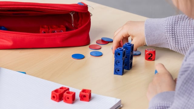 Mädchen hat auf dem Tisch vor sich einen Rechenschieber, Würfel und einen Schreibblock