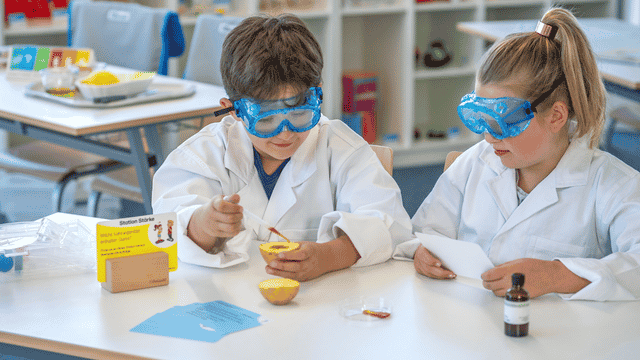 Zwei Kinder mit Schutzbrillen experimentieren im Klassenzimmer