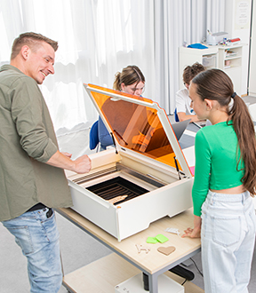 Kinder und ein Lehrer sitzen/stehen um einen Tisch mit Laser