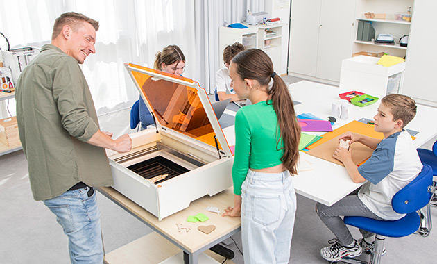 Kinder und ein Lehrer sitzen/stehen um einen Tisch mit Laser